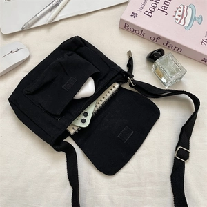 Internal storage view of black canvas crossbody bag showing phone and earphone pockets