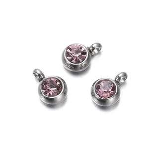 Detailed view of silver stainless steel pendants with round pink zircon crystals on white background