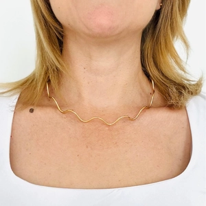 Minimalist 18K gold wave pattern necklace on model neck with polished metal finish