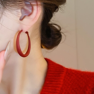 Close-up of a matte dark red C-shaped hoop earring on model with red knitwear