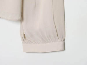 Detail of elegant beige blouse sleeve featuring delicate pleated cuffs and vertical texture