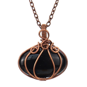 Close-up of handmade wire wrapped black gemstone pumpkin pendant on bronze necklace chain