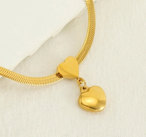 Macro detail of golden snake chain necklace featuring two polished heart pendants