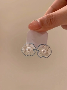 Detailed macro view of silver hollow flower pearl earrings with elegant blue enamel accents