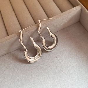 Detail of silver wavy J-shape earrings with a liquid metal finish on beige velvet tray