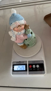 Close-up of ceramic Christmas boy figurine weight measurement on a scale at 252.6g