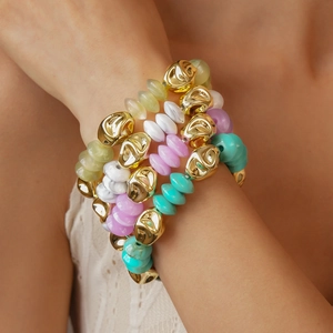 Detail of layered acrylic beaded bracelets with irregular gold metal pieces on a wrist