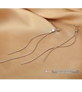 Macro shot of silver tassel earrings with snake chains on champagne silk fabric