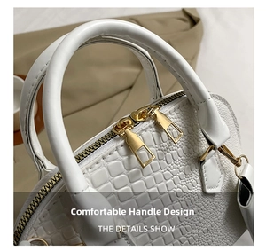Detail of white embossed shell bag featuring dual gold zippers and sleek round handles