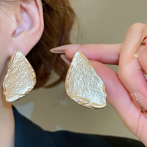Detailed view of large gold-tone irregular earrings with unique hammered texture surface