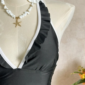 Detailed view of black swimsuit featuring white ruffles and a stylish halter neckline