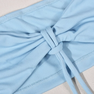 Détail d'un crop top en maille bleu clair avec nœud central torsadé et lacets