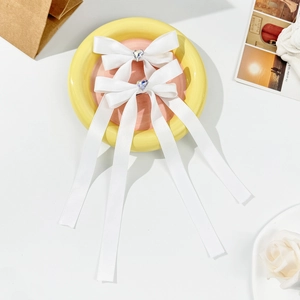 White ribbon bow hair clips with heart-shaped crystal center on decorative yellow plate