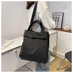 Detailed view of a black minimalist nylon tote bag with shoulder straps worn by a model