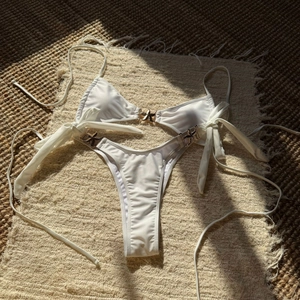 Detailed view of white bikini with gold starfish charms and halter straps on a beach mat