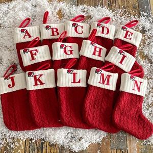 Knitted red Christmas stockings with white alphabet embroidery on snowy wood background