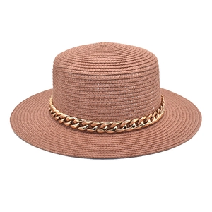 Détail du chapeau en paille marron à bord plat avec une chaîne décorative en métal doré