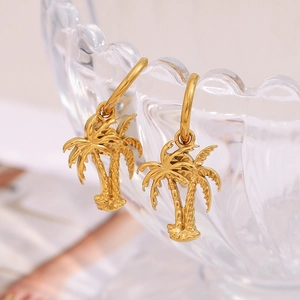 Detailed view of gold coconut tree charm earrings on a magazine and glassware backdrop