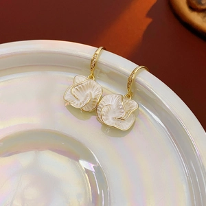 Detailed view of white enamel flower earrings with gold plating on a ceramic tray