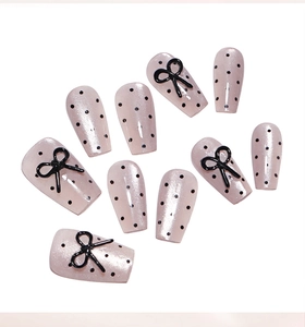 Detail of sweet pink press-on nails with black polka dots and 3D bow ornaments