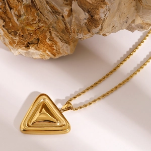 Detail einer goldenen Kordelkette mit einem geometrischen Dreiecksanhänger auf Naturstein