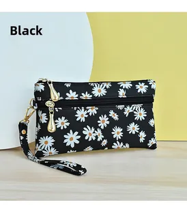 Detail of black daisy print handbag with gold zippers and wristlet strap on a wooden desk