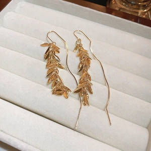 Macro shot of gold-plated leaf tassel earrings on a soft cream jewelry display