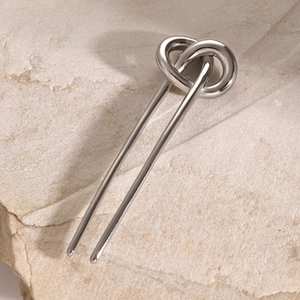Detailed view of a silver stainless steel knotted hair pin on a textured stone surface
