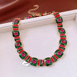 Dettaglio di collana vintage dorata con smalto verde e perle rosse sulla seta
