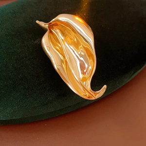 Detail of a golden leaf-shaped metal brooch resting on dark green velvet fabric
