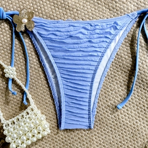 Detail of light blue bikini bottom with ribbed fabric, metallic flower and pearl accent