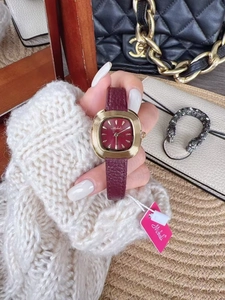 Close-up of a luxury gold square watch with a burgundy leather strap on a woman's wrist