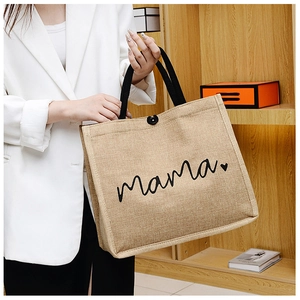 Detail of light brown linen tote bag featuring 'mama' text and black fabric handles