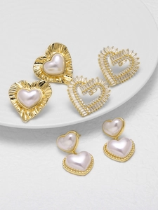 Detalle de pendientes de corazón dorados con perlas y circonitas cúbicas pavé