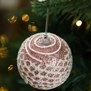 Pink glitter Christmas ball with white weave detail hanging on a festive tree