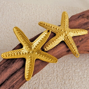 Pair of gold starfish pendants made of 304 stainless steel on dark wood and sand