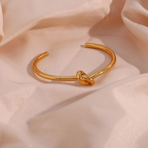 Macro detail of 18K gold plated stainless steel knot bracelet on satin background