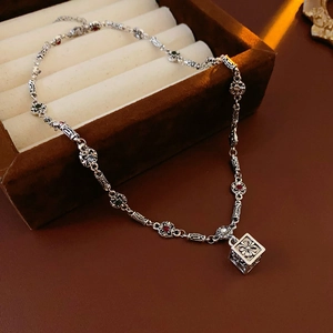 Close-up of vintage silver necklace with hollow cube pendant and colorful gemstones