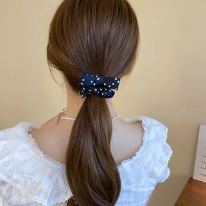 Rear view of cream polka dot bow scrunchie styled on a low ponytail with lace shirt