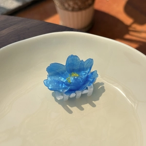 Blue translucent acrylic flower hair claw clip on a white plate with soft shadows