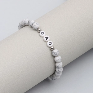 Close-up of white marble beaded bracelet featuring DAD letter charms on a display stand