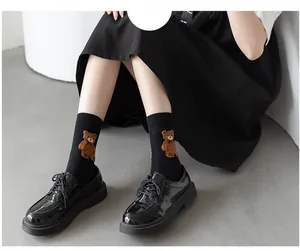Detail of black crew socks with 3D brown bear pattern and glossy patent leather loafers