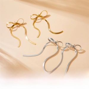 Detail of gold and silver bow tassel earrings with snake chain fringe on beige background