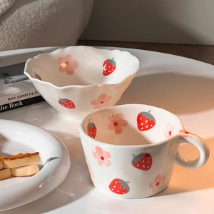 Macro shot of hand-painted strawberry ceramic mug and bowl with wavy edges for breakfast