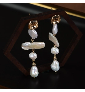 Macro detail of long Baroque pearl earrings with gold plating on a dark display stand