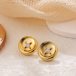 Close-up of golden button earrings with square zircon on a beige mesh fabric background