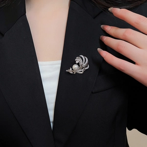Dettaglio della spilla a piuma con zirconi e perla bianca su un blazer nero elegante