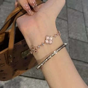 Close-up of rose gold clover bracelet and diamond bangle worn by model with handbag