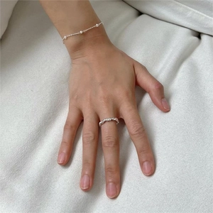 Close-up of minimalist knot ring and delicate pearl bracelet on textured fabric