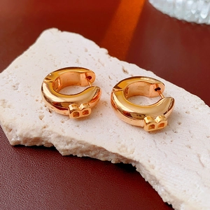 Detailed close-up of golden hoop earrings with B letter pendant on beige stone